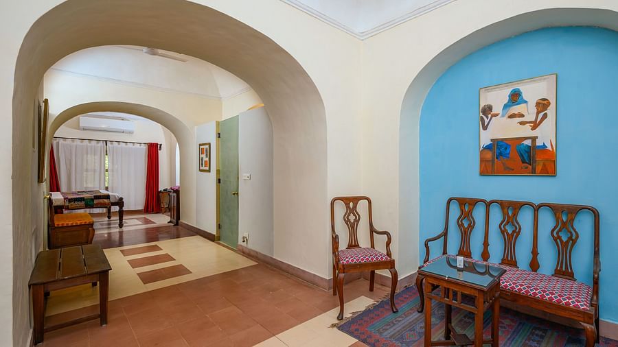 A hotel room with arched openings, chairs, a small table, artwork, and a view into a room with a desk at Tijara Fort-Palace, Alwar.