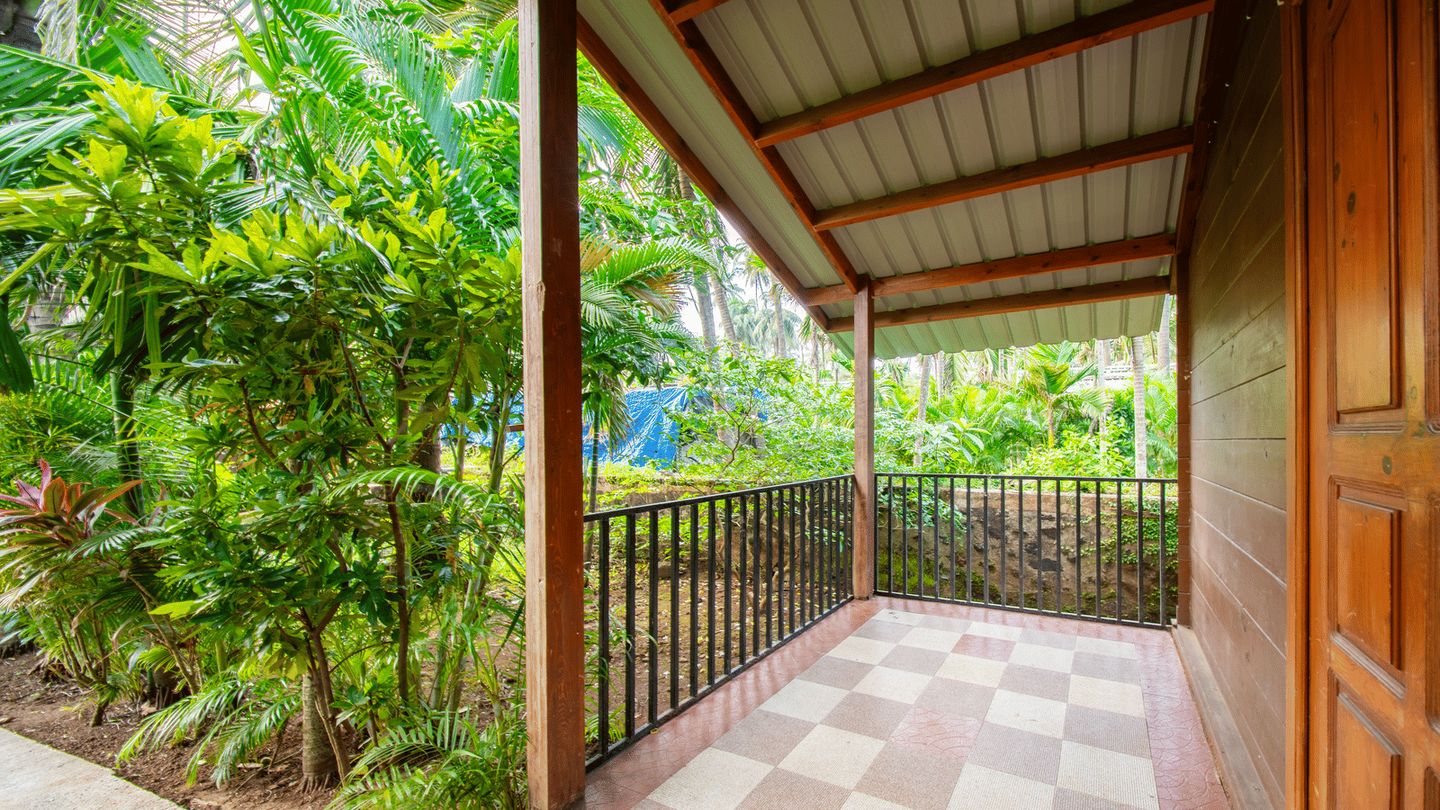 Porch with tile floor, roof, and surrounding plants at Tranquil Beach Resort, Harihareshwar.