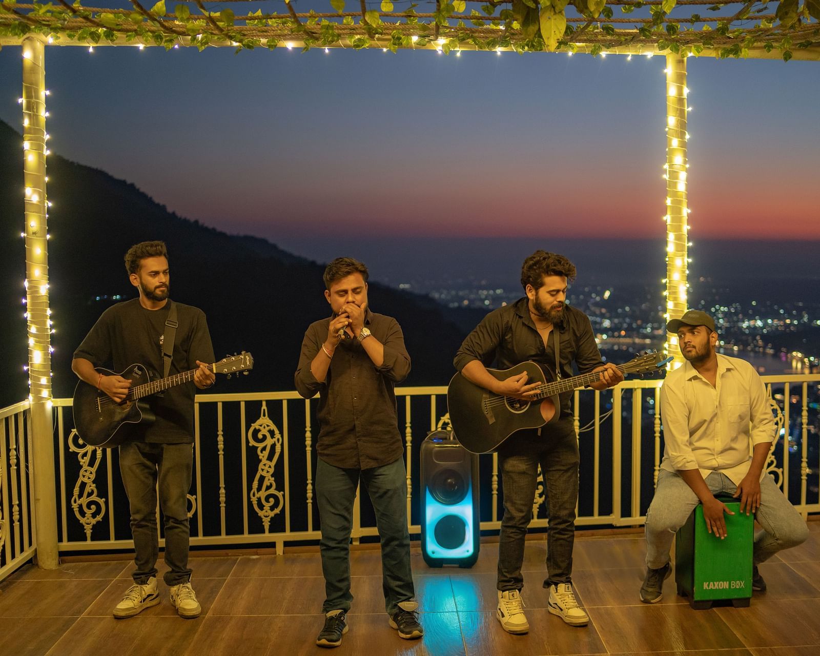 A wide-angle view of the rooftop area at Neer Ganga after sunset, with live music creating a vibrant atmosphere. where people are playing different instrument and singing song at Neer ganga.