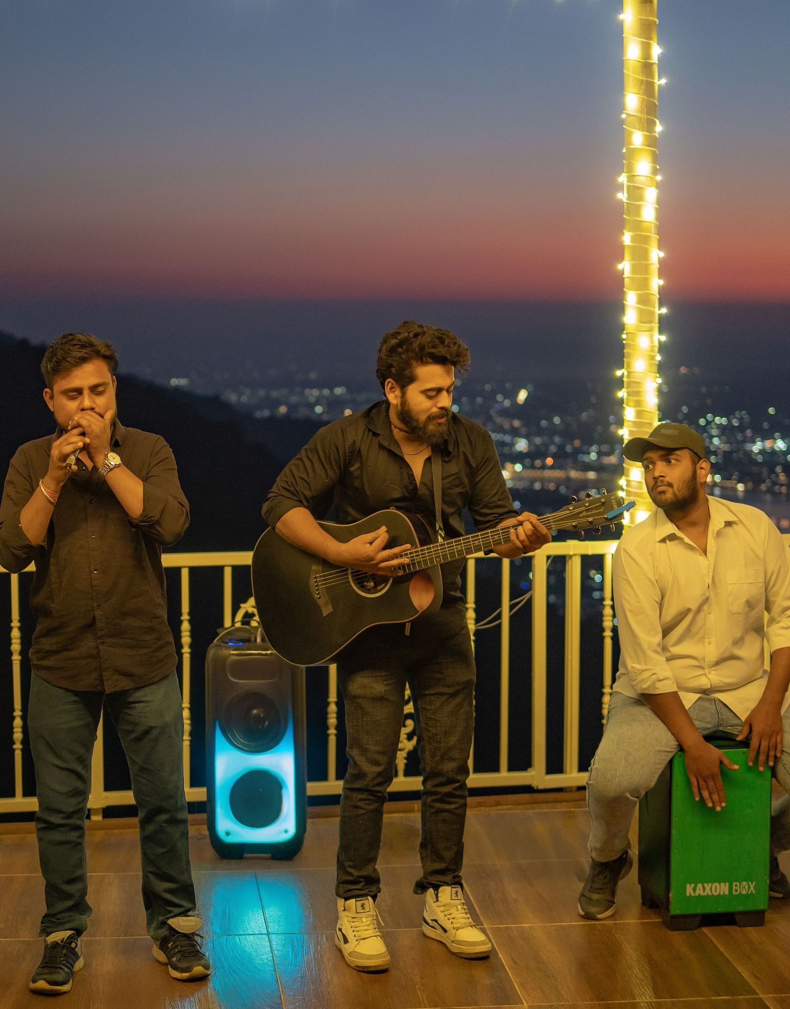 A wide-angle view of the rooftop area at Neer Ganga after sunset, with live music creating a vibrant atmosphere. where people are playing different instrument and singing song at Neer ganga.