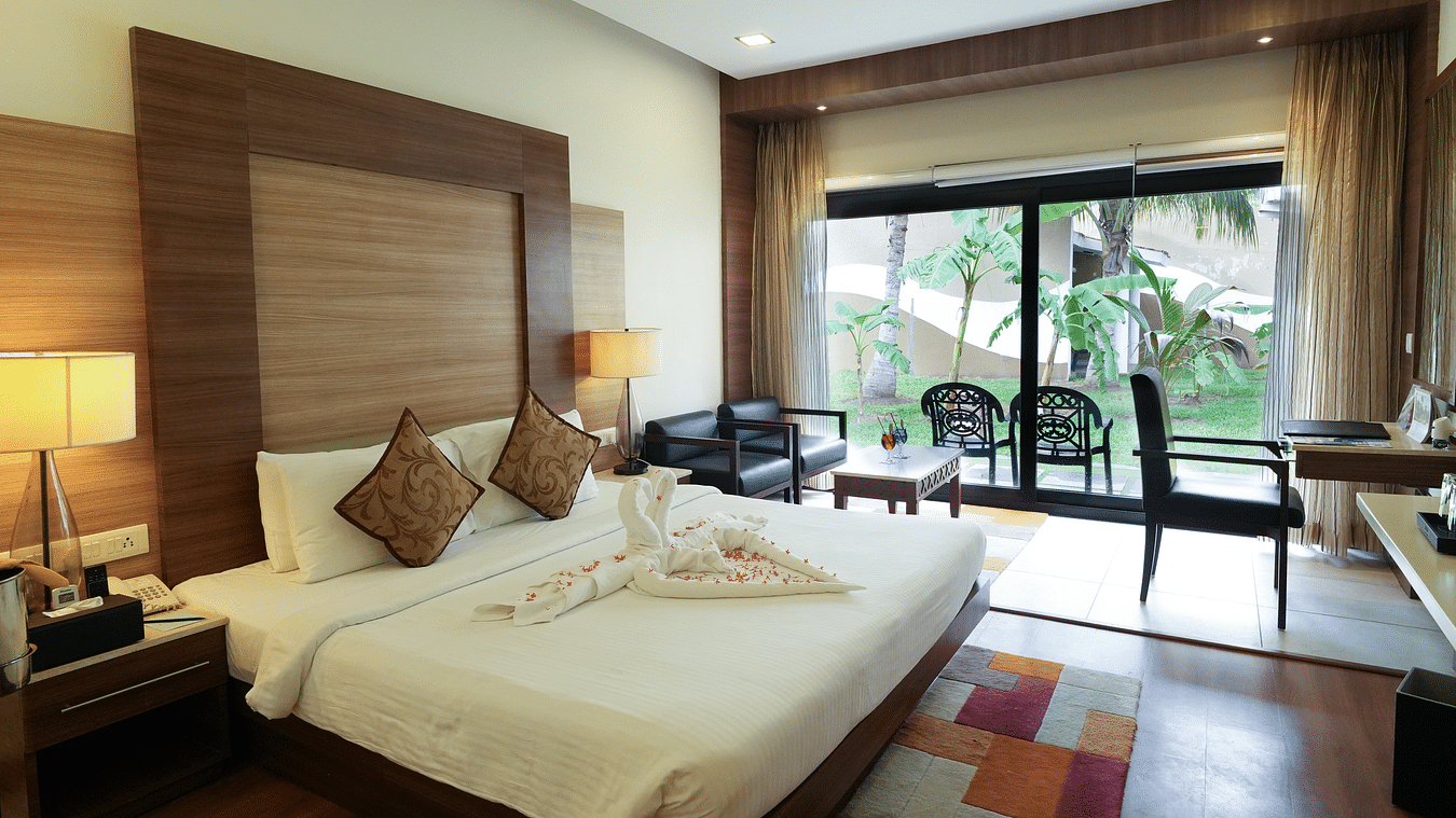 A clean and cozy hotel room with a neatly made bed, a study desk with a chair, and a balcony that opens to a green lawn. The room has nice furniture and a warm atmosphere - MGM Beach Resorts