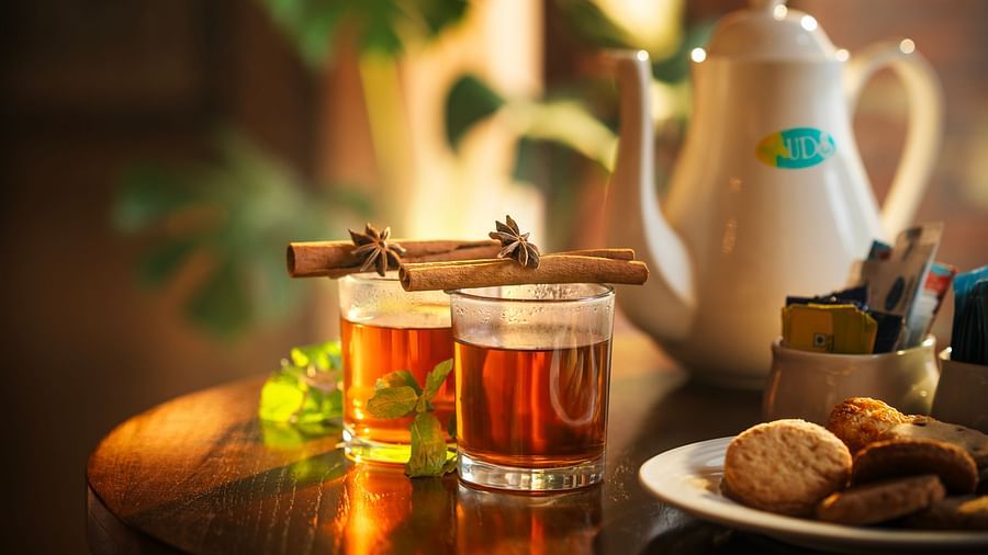Two glasses of tea with mint leaves on the side and cinnamons placed on the top of the rims while cookies and sachets of sugars are placed next to the kettles at Uday Backwater Resort