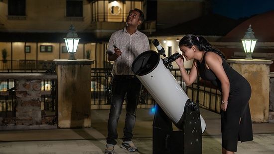 An image of one person stargazing through a telescope, with another person standing beside. 
