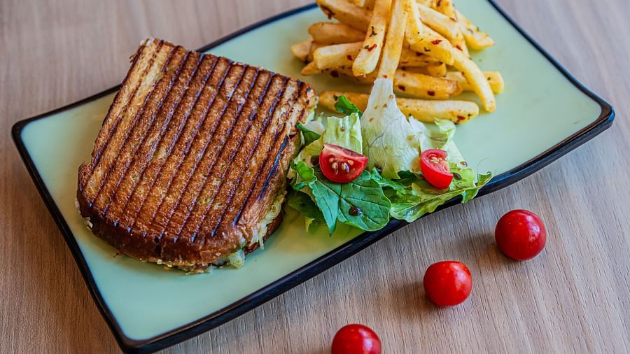 A rectangular plate with a sandwich and vegetables on the side, accompanied by French fries and mini tomatoes placed beside the plate at Indie Stays Mumbai International Airport.