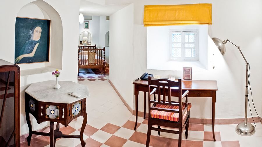 A room with tables, a chair, a lamp, and a doorway leading to another room in Tijara Fort-Palace - 19th Century, Alwar.