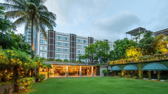 Facade view of Kenilworth Hotel with the banquet hall in Park Street, Kolkata, featuring a lawn area, potted plants having fairy lights on it, and a trees on either side of the building.