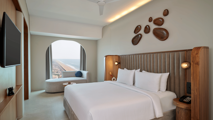 The Oasis Suite at Swosti Premium Beach Resorts, Puri, with a double bed, a television mounted on the wall, artistic wall decor, a window, and wooden headboard.