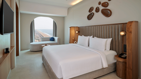 The Oasis Suite at Swosti Premium Beach Resorts, Puri, with a double bed, a television mounted on the wall, artistic wall decor, a window, and wooden headboard.