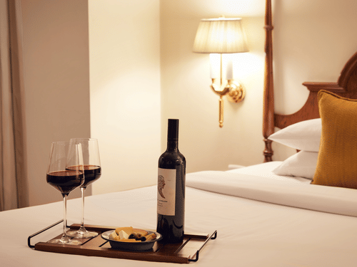 A bottle and two glasses of wine on a bed at the finest Hotels in Juhu - Ramada Plaza Palm Grove