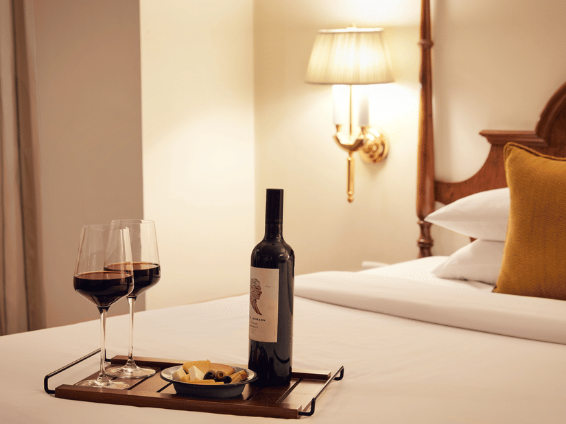 A bottle and two glasses of wine on a bed at the finest Hotels in Juhu - Ramada Plaza Palm Grove