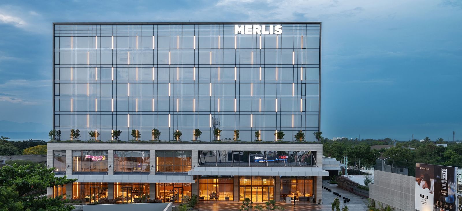 Full exterior view of the hotel building during twilight, showcasing its modern design at Merlis Hotel, the best 5-star hotel in Coimbatore and one of the Best Marriage Halls in Coimbatore.