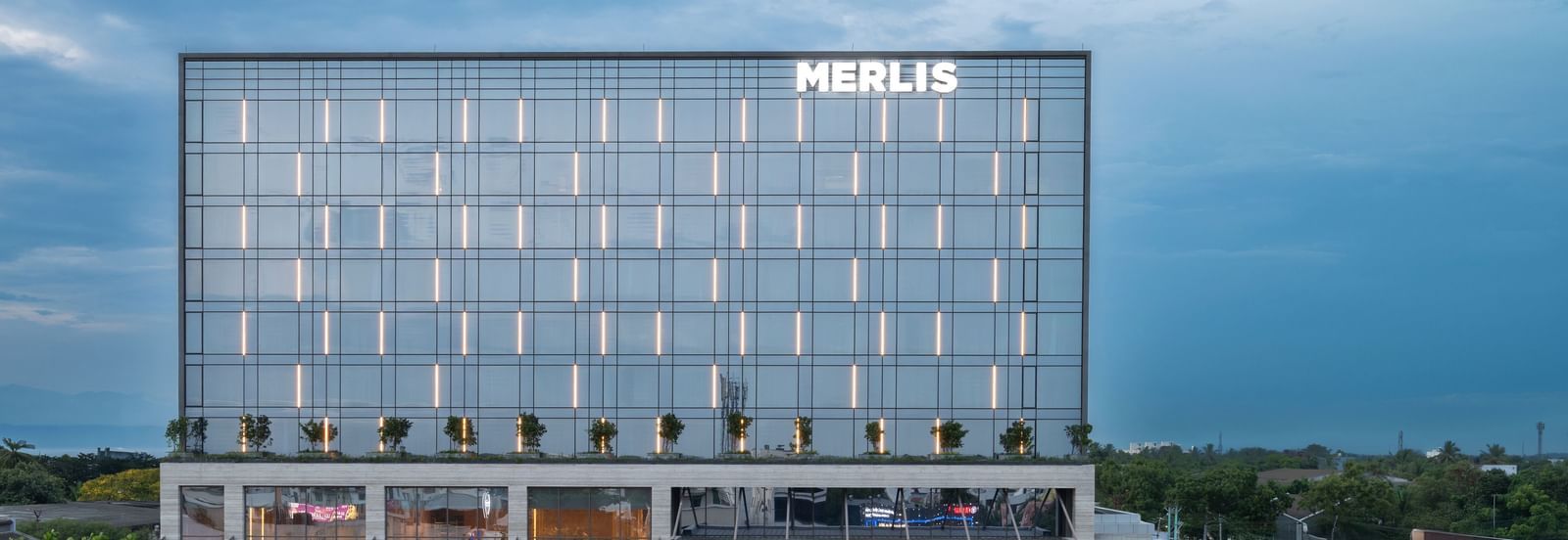 Full exterior view of the hotel building during twilight, showcasing its modern design at Merlis Hotel, the best 5-star hotel in Coimbatore and one of the Best Marriage Halls in Coimbatore.