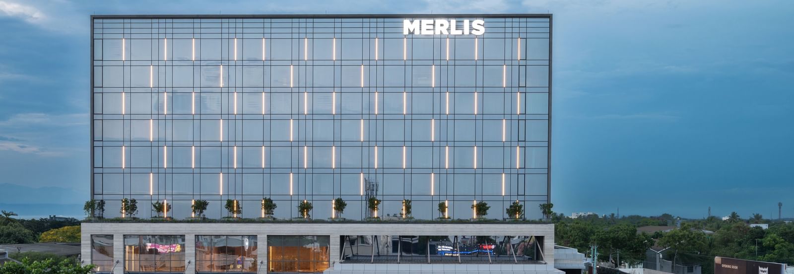 Full exterior view of the hotel building during twilight, showcasing its modern design at Merlis Hotel, Coimbatore.
