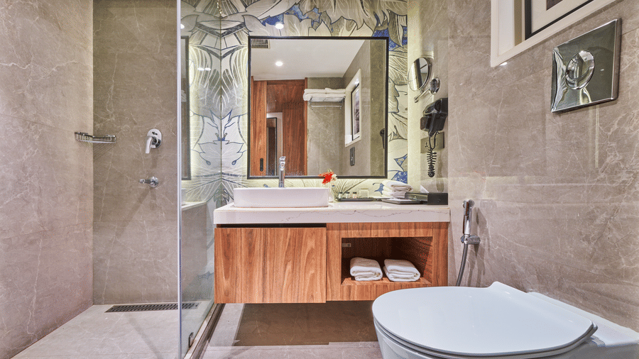 A bathroom featuring a wooden vanity with a white sink, a large mirror, and a white toilet | HHI Varanasi