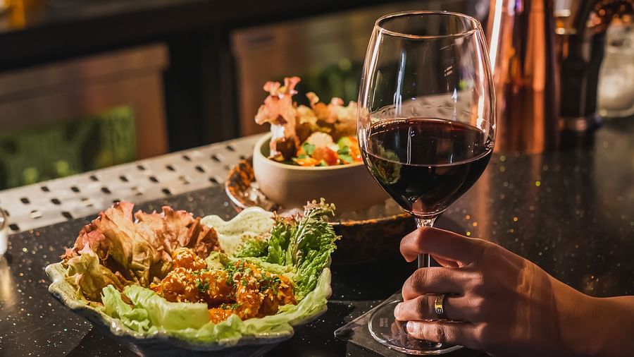 image of a person holding a glass of wine along with a delicious serving on the table at The Claridges New Delhi