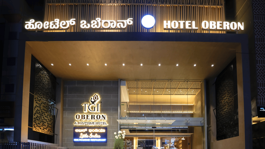 Hotel Oberon entrance with signage in Kannada and English, modern architectural design, steps leading to the main door, and potted plants on either side.