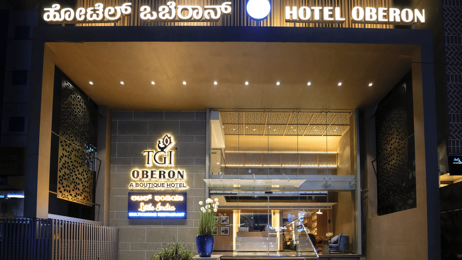 Hotel Oberon entrance with signage in Kannada and English, modern architectural design, steps leading to the main door, and potted plants on either side.