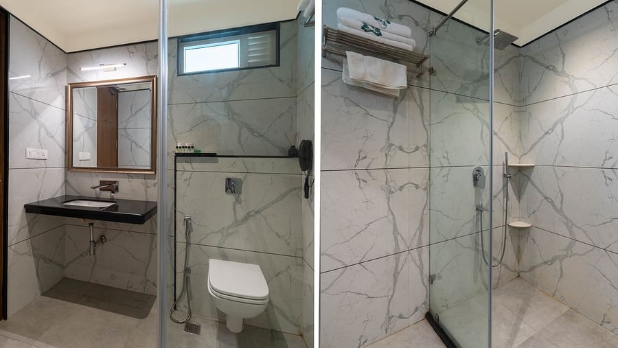 A spacious bathroom featuring a wall-mounted mirror above the washbasin, a western toilet to the side, and a glass partition separating the shower area Panna Vilas Palace