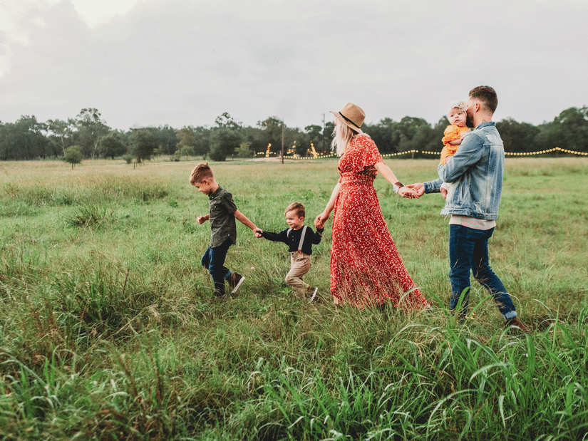 A group of people walk in a field, and two children accompanying.