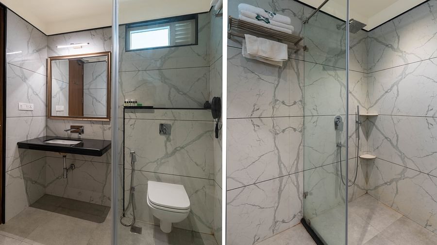 A spacious bathroom featuring a wall-mounted mirror above the washbasin, a western toilet to the side, and a glass partition separating the shower area Panna Vilas Palace