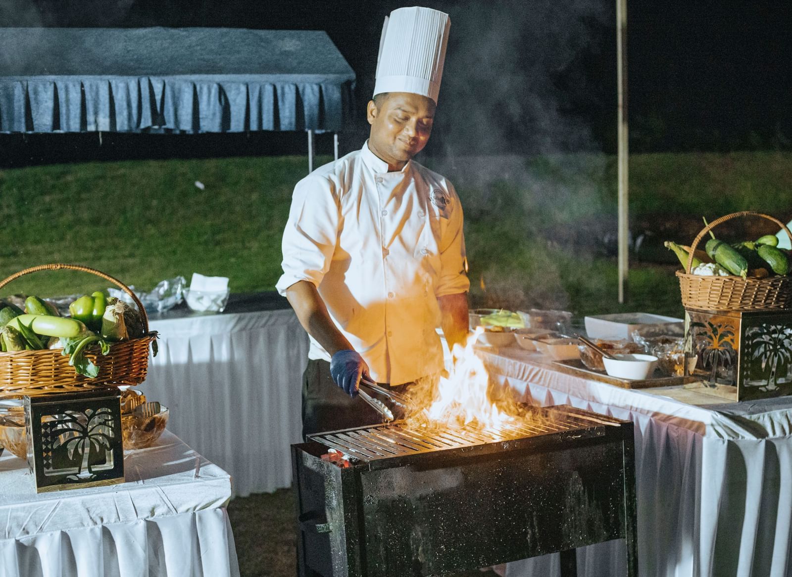 Chef cooking with open flames on a live grill counter in an outdoor setting at Fireflies Resorts, Kabini.