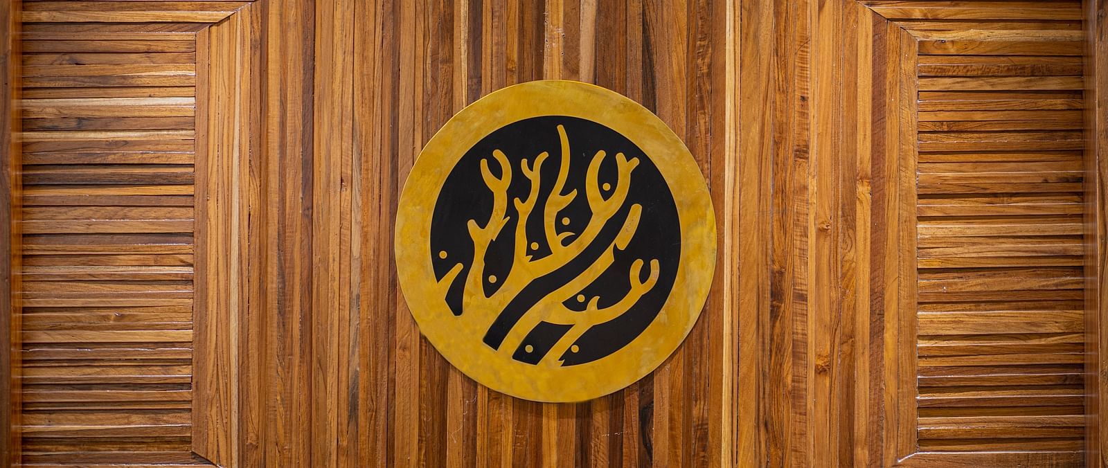 A close-up of a logo featuring abstract shapes on a wooden background - Coral Reef Hotel & Spa, Port Blair