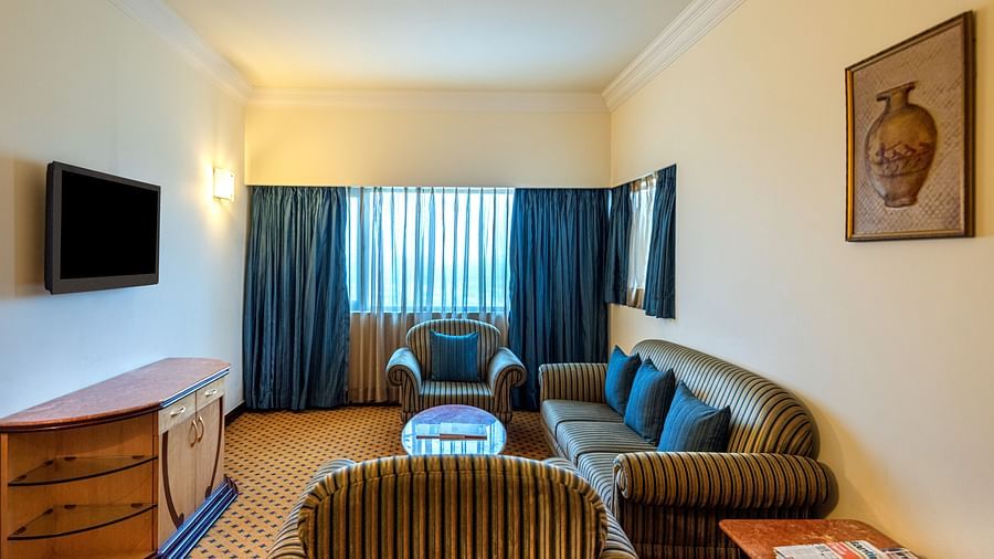 An image of a seating area with sofa sets, centre table, flat TV screen, and a cabinet in a Deluxe Suite - The Suryaa New Delhi