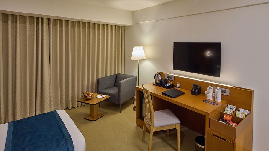 a television, desk with a tea/coffee maker, and a sofa with a coffee table beside twin beds in The Grand Deluxe Twin at Grand Continent, Mahabalipuram