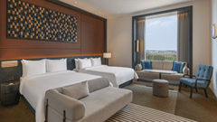 Premium Family Room at The Residency Signature Madurai featuring two double beds, a small gray sofa, a window seating area, and a large decorative wall panel.
