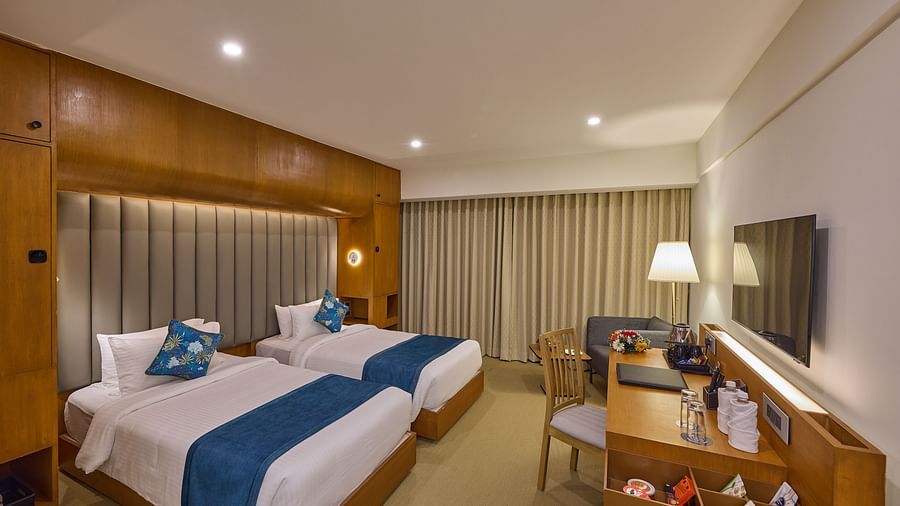 twin beds beside television over a desk with snacks kept on it in The Grand Deluxe Twin at Grand Continent, Mahabalipuram