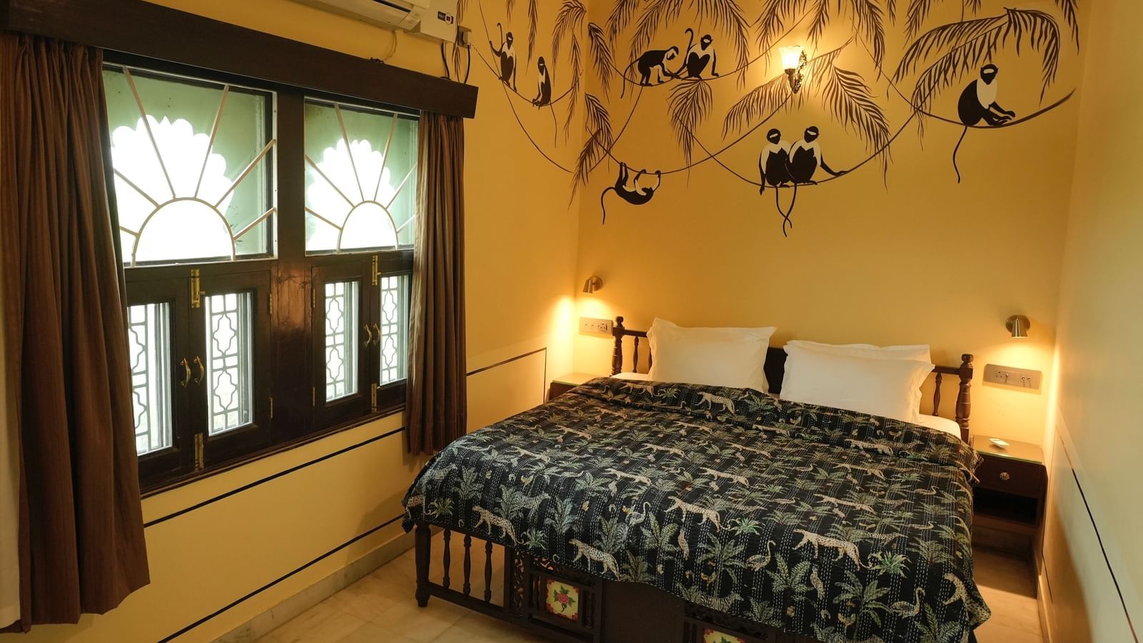 A grand bedroom in the Terrace Suite at Mahendra Niwas, featuring a large bed with a decorative headboard and white bedding. A chandelier hangs from the ceiling.