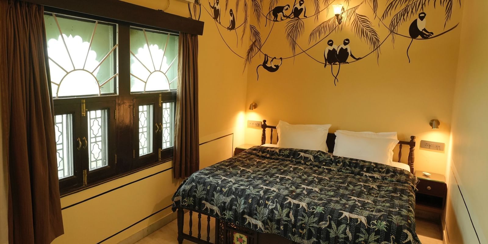 A grand bedroom in the Terrace Suite at Mahendra Niwas, featuring a large bed with a decorative headboard and white bedding. A chandelier hangs from the ceiling.