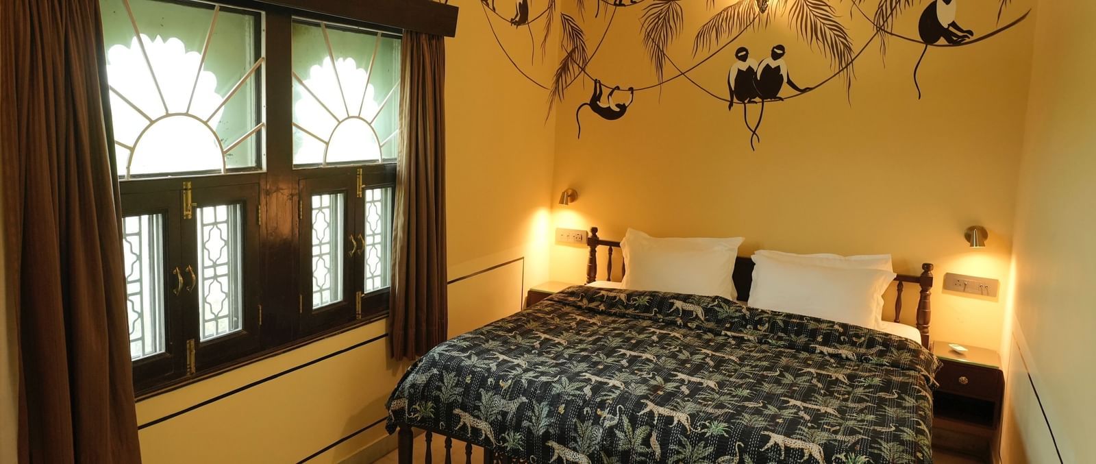 A grand bedroom in the Terrace Suite at Mahendra Niwas, featuring a large bed with a decorative headboard and white bedding. A chandelier hangs from the ceiling.