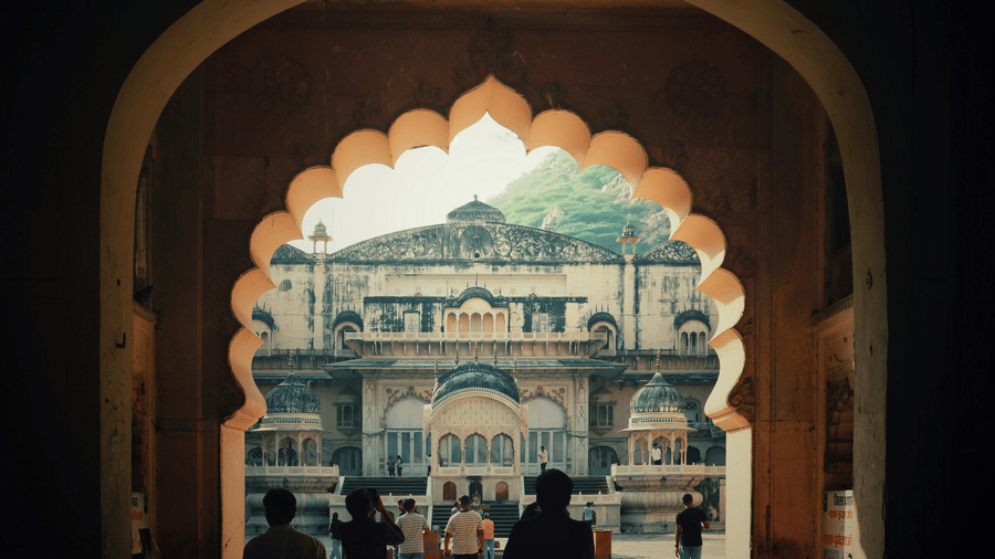 Visitors walking through an arched entrance into a grand heritage palace courtyard.