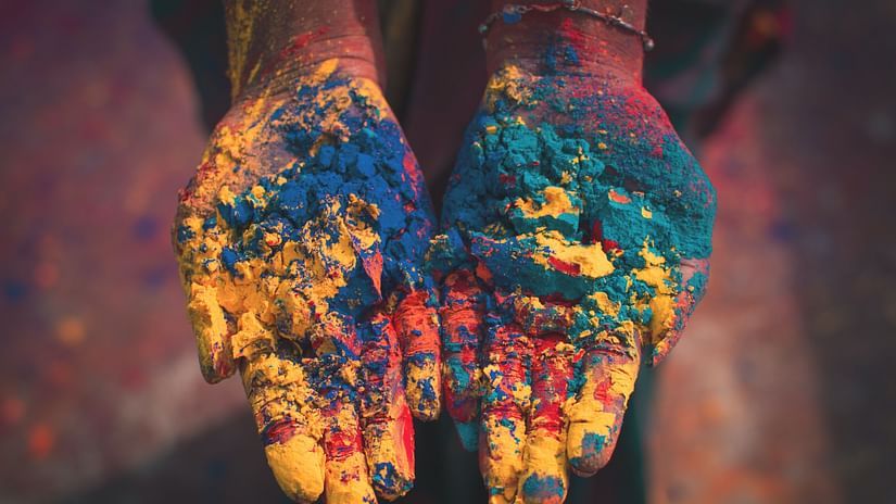 a person showing their palms for a picture with different holi colours etched on the palm