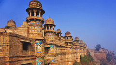 A facade of the Gwalior Fort featuring its architecture as the sun falls on its walls under a clear blue sky