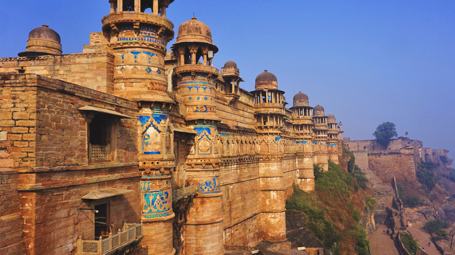 A facade of the Gwalior Fort featuring its architecture as the sun falls on its walls under a clear blue sky