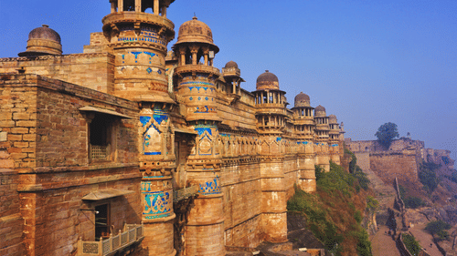 A facade of the Gwalior Fort featuring its architecture as the sun falls on its walls under a clear blue sky