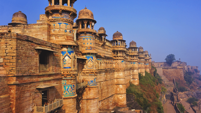 A facade of the Gwalior Fort featuring its architecture as the sun falls on its walls under a clear blue sky