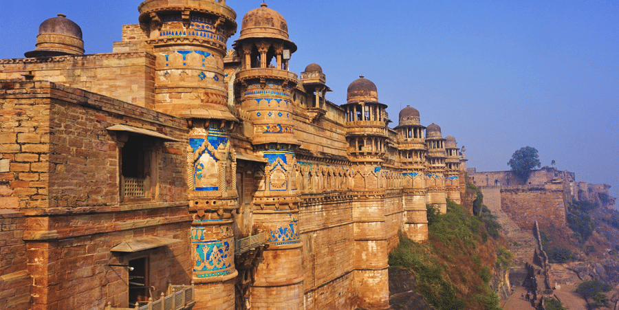 A facade of the Gwalior Fort featuring its architecture as the sun falls on its walls under a clear blue sky