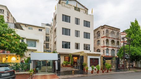 A wide-angle daytime shot of the hotel's exterior, showcasing the multi-storey, local street surroundings, and a clear sky - Amantra Comfort Hotel