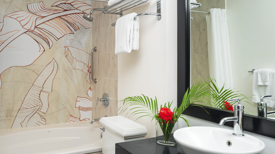 modern, well-lit bathroom featuring a  sink on a countertop, a large mirror, a toilet, and a glass-enclosed shower with decorative tiling. A small vase with flowers sits on the counter, and fresh towels are folded on a rack above the toilet in  S Hotels Ki