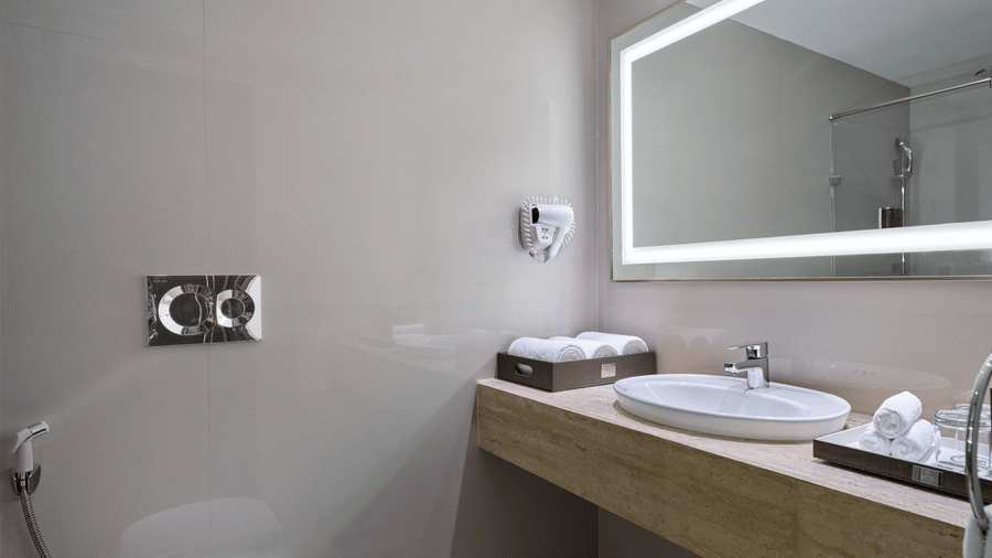 The bathroom of Club Room at Swosti Premium, Bhubaneswar, featuring a sink, toileteries, a toilet, and a mirror.