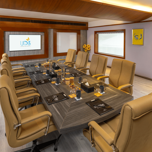 A boardroom featuring chairs around a table with a mug, notepad, pen, and water glass on the surface, along with a presentation screen at the front at Uday Samudra Leisure Beach Hotel