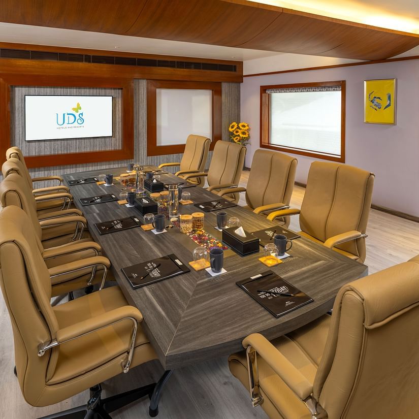 A side view of a boardroom featuring chairs around a table with a mug, notepad, pen, and water glass on the surface, along with a presentation screen at the front - Uday Samudra Leisure Beach Hotel