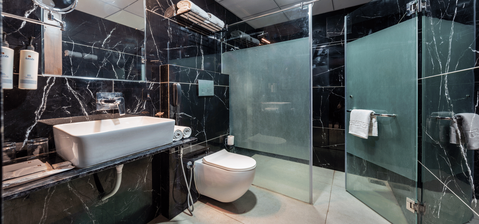 Luxurious black marble bathroom with a freestanding bathtub and glass shower enclosure at Lords Studio Inn, Jamnagar.