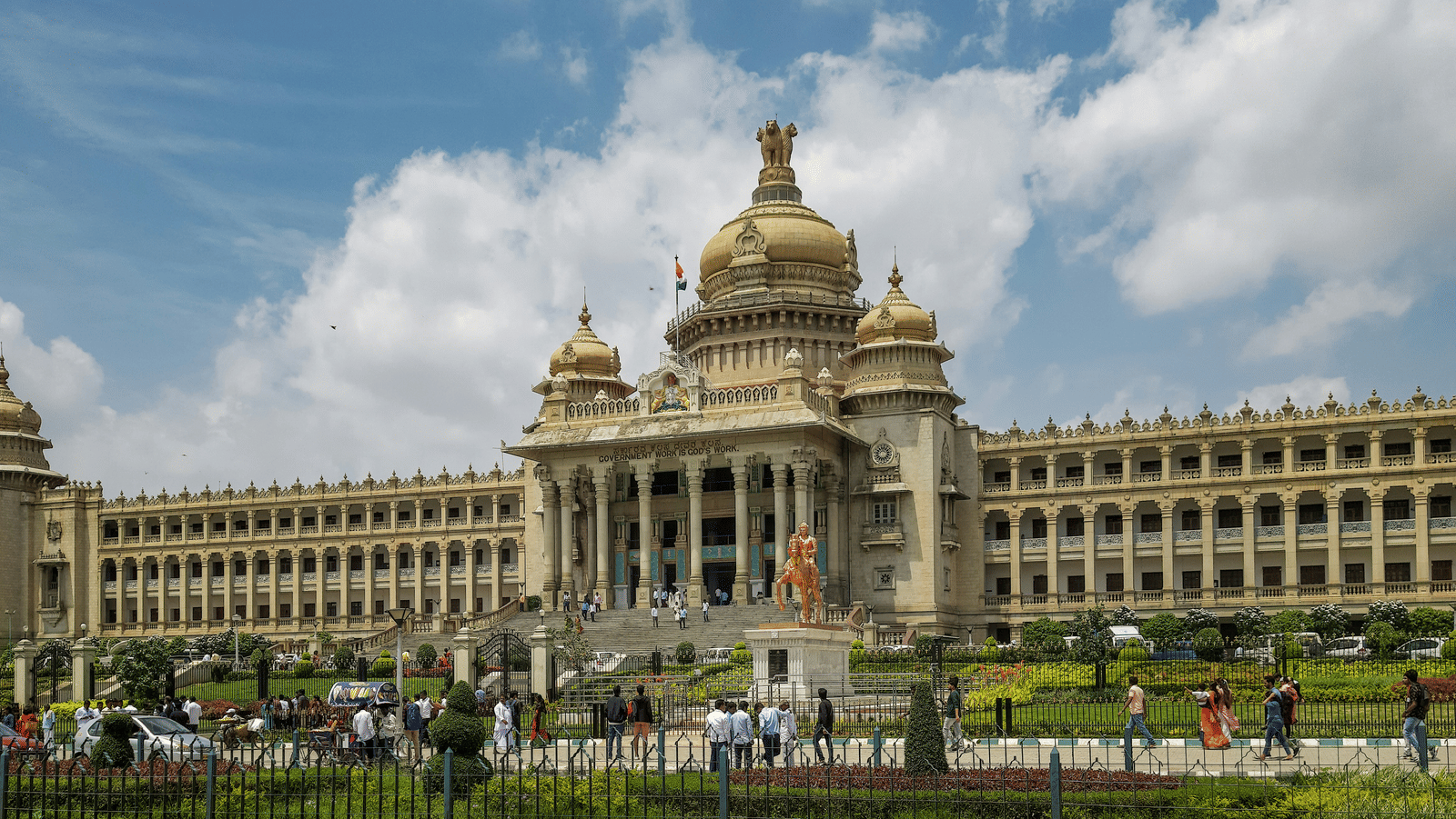 A magnificent stone building with grand columns and domes situated behind a large green lawn.