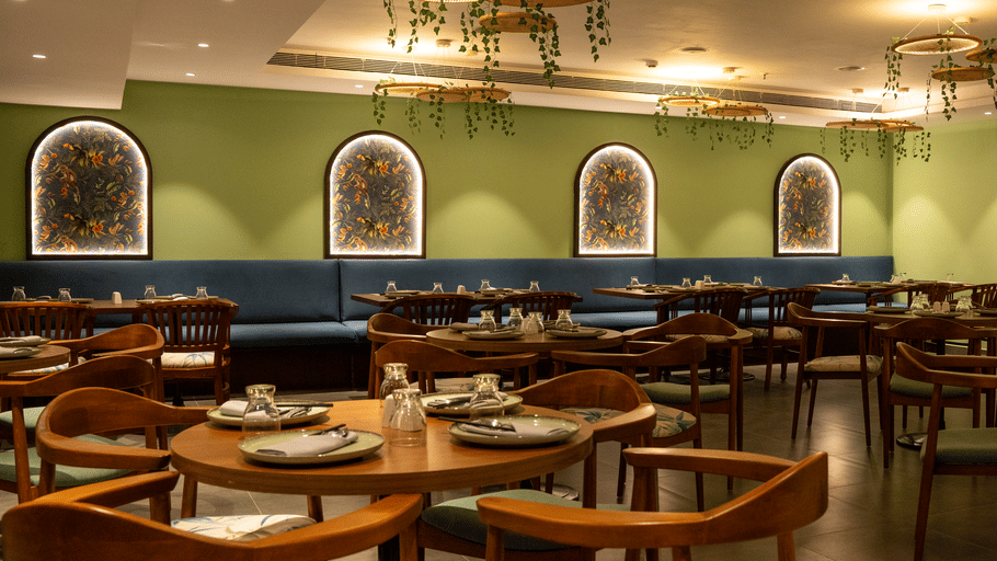 Spacious dining area with arched wall panels, wooden chairs and warm ambient lighting at OJ Japanese Restaurant, Featherlite Evoma Hotel.