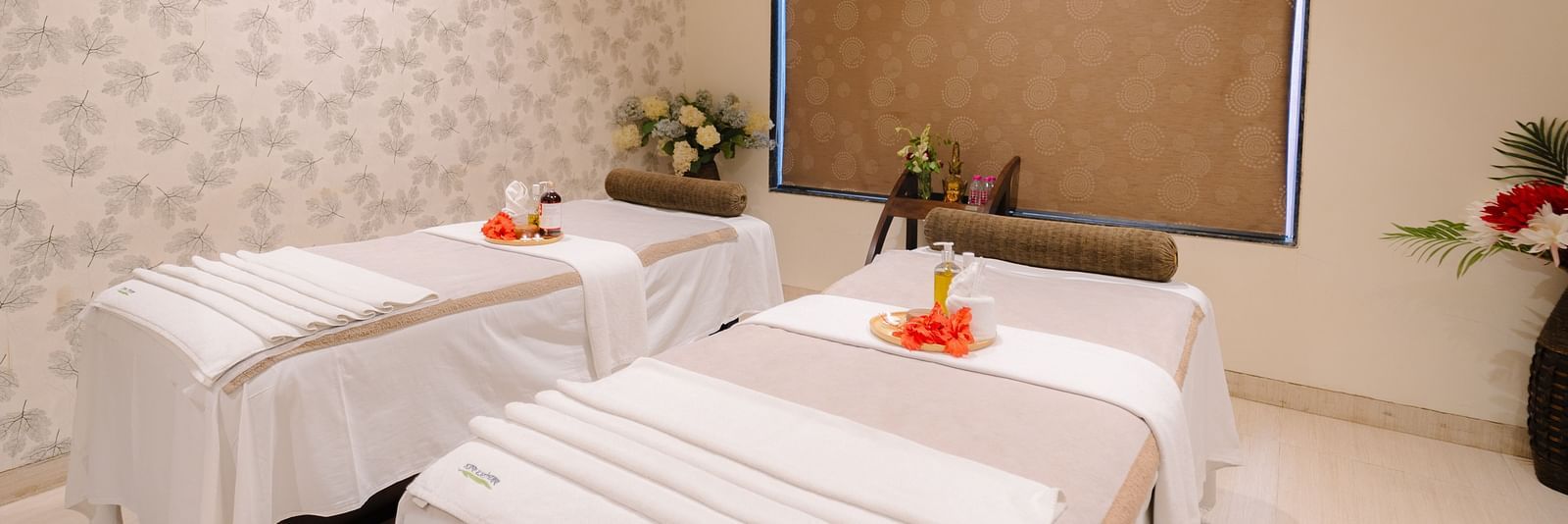 Two spa beds neatly made and adorned with flowers, with all the necessary equipment arranged on the table at Crescent spa & resort, Indore
