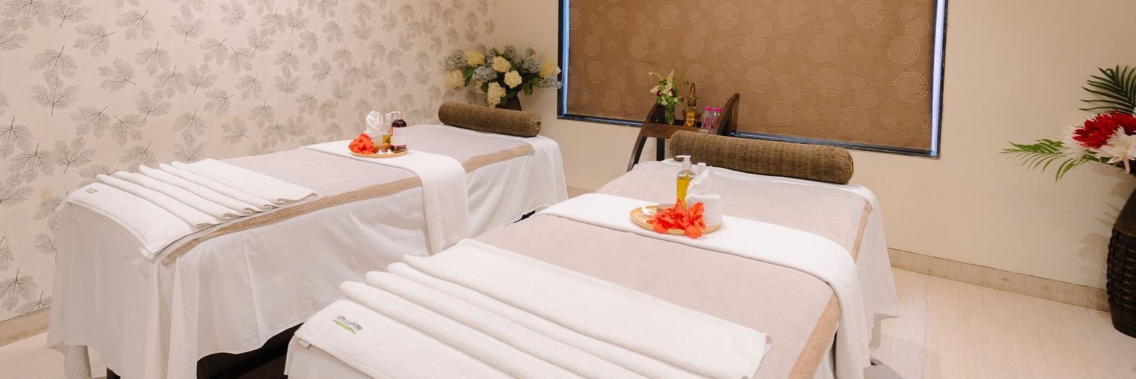 Two spa beds neatly made and adorned with flowers, with all the necessary equipment arranged on the table at Crescent spa & resort, Indore